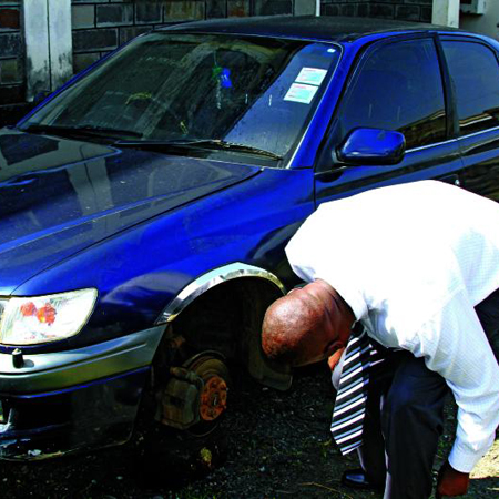 Standard Group Nakuru region Advertising Manager Joseph Yego inspects his vehicle which was vandalized by robbers inside his compound on Monday night.They stole two wheels and other accessories.